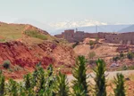 Ourika village on a red eroded hillside with snow-capped High Atlas peaks in the background