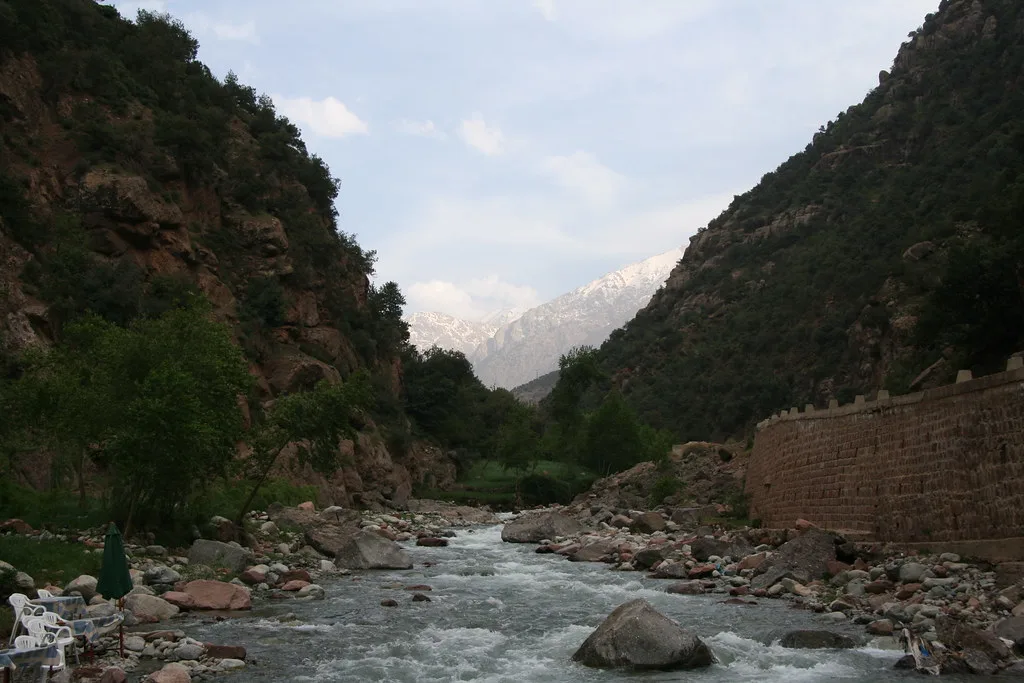 Riverside café terrace in the Ourika gorge, rock walls and a snow-capped peak in view Riverside café terrace in the Ourika gorge, rock walls and a snow-capped peak in view