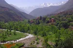 Ourika Valley in bloom, with a river winding past a red-walled village below the snow-capped High Atlas peaks