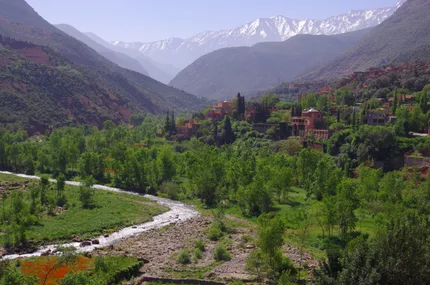 Ourika Valley in bloom, with a river winding past a red-walled village below the snow-capped High Atlas peaks