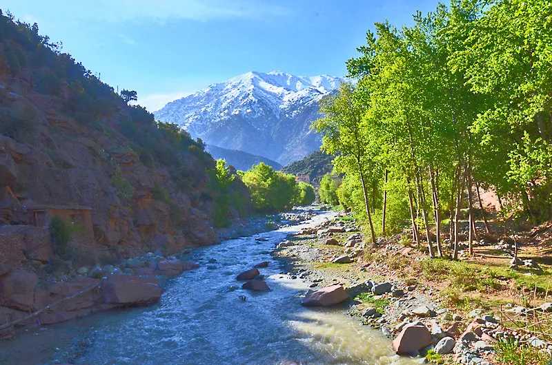 Ourika River flowing beneath canyon walls, with a snow-capped peak in the distance Ourika River flowing beneath canyon walls, with a snow-capped peak in the distance