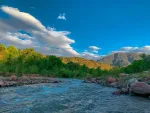 Ourika River rushing past green hills with the High Atlas Mountains in the distance