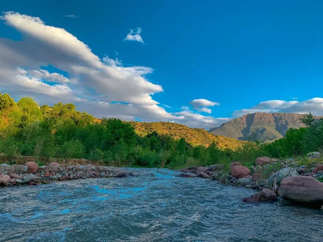 Ourika River rushing past green hills with the High Atlas Mountains in the distance Ourika River rushing past green hills with the High Atlas Mountains in the distance