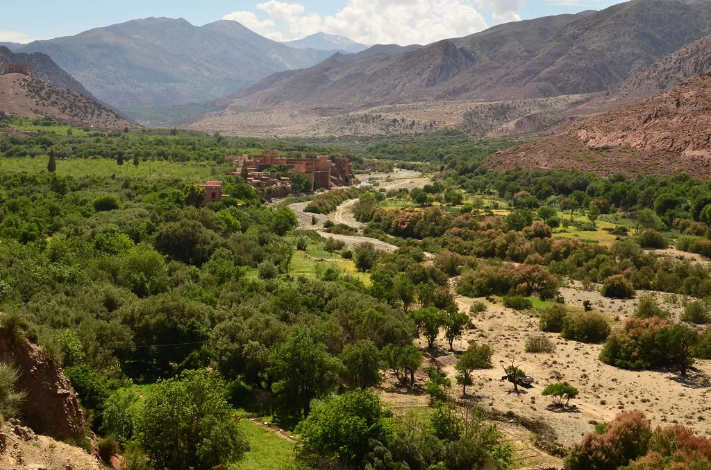 Kasbah-style buildings surrounded by greenery in the Asni Valley, with snow-capped Atlas peaks beyond Kasbah-style buildings surrounded by greenery in the Asni Valley, with snow-capped Atlas peaks beyond