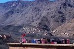 Rooftop with drying laundry and a Moroccan flag, overlooking a distant Berber village on the mountainside