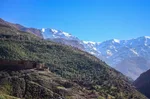 Terraced green hillside above Imlil descending toward a range of snow-capped High Atlas peaks