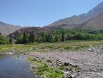 Mountain stream and green fields leading to an Imlil village nestled among trees, with High Atlas peaks behind