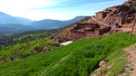 Terraced red mudbrick Berber village on a hillside above a green valley in Ouirgane, with a car climbing the mountain track