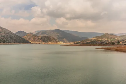 Ouirgane Lake glowing turquoise beneath dramatic clouds, with High Atlas foothills rising along both shores