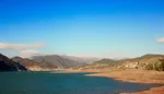 Ouirgane Lake under a clear blue sky, with exposed sandy shoreline and hills beyond